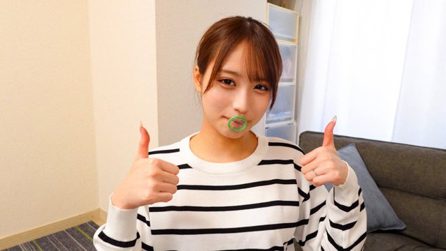 ソファの前でボーダーニット姿の女性が緑のコンドームを口元に当て、両手で親指を立てる